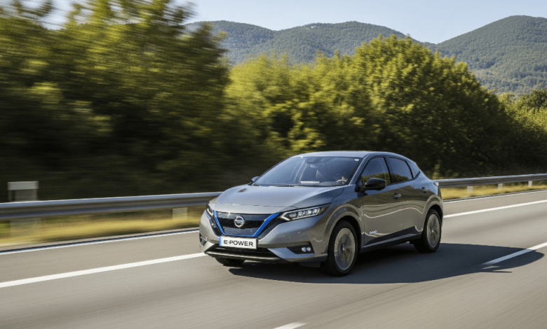 A Nissan e-Power hybrid car driving smoothly on a highway surrounded by greenery