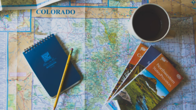 Map of Colorado surrounded by travel essentials including a notebook, pencil, coffee cup, and AAA travel guides, illustrating the Ultimate Travel Checklist.
