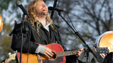 Sean Feucht speaking at a large outdoor worship rally with flags and supporters in the background
