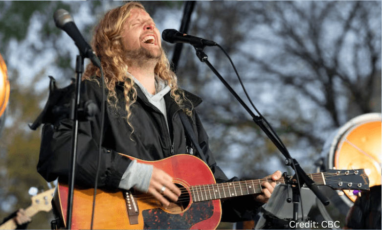 Sean Feucht speaking at a large outdoor worship rally with flags and supporters in the background