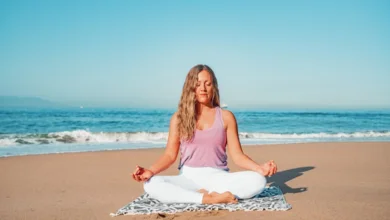 Woman practicing meditation on the beach to reduce stress and improve mental well-being.