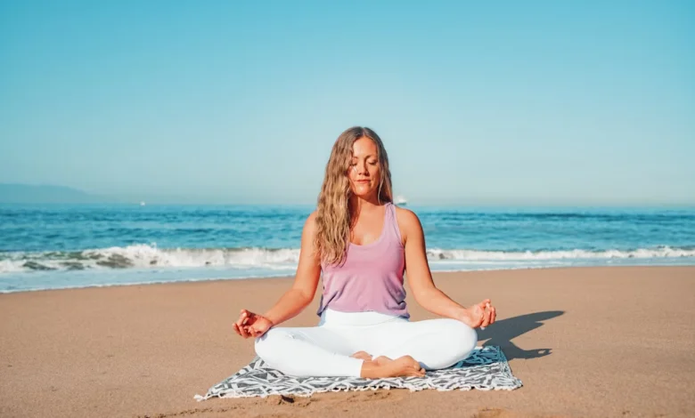 Woman practicing meditation on the beach to reduce stress and improve mental well-being.