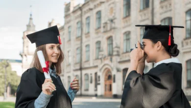 best colleges in British Columbia two graduates in caps and gowns celebrating with a diploma outside a historic campus building.