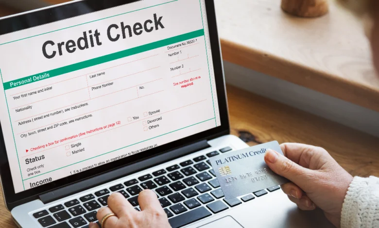 Person checking credit score in Canada on a laptop while holding a credit card and reviewing financial details